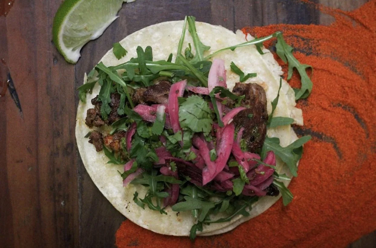 Overhead carne asada taco with pickled onion, arugula and lime